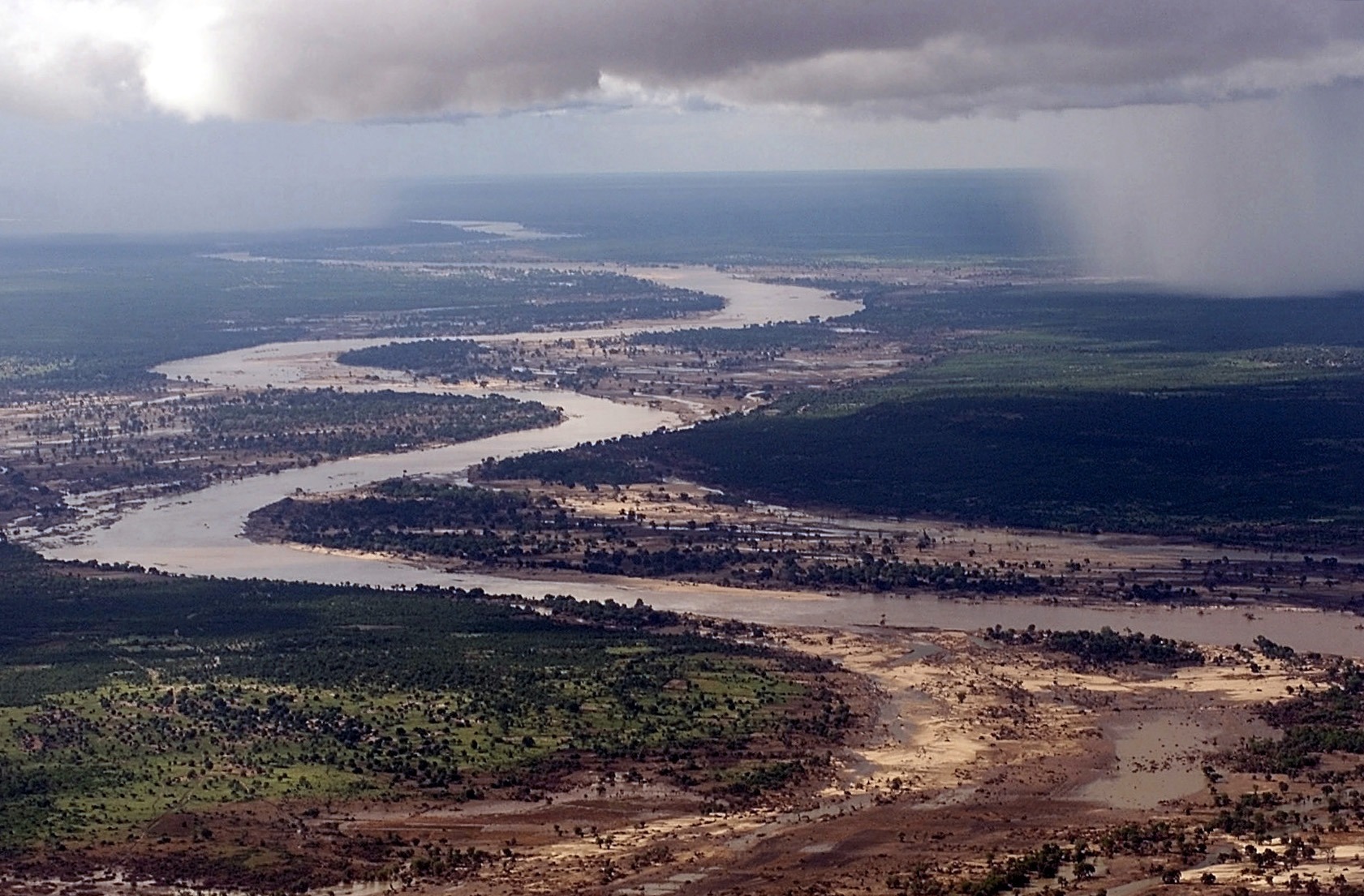 Aerial view, extreme long shot, looking down as the Limpopo River winds its way through Southern Mozambique, where it recently crested its banks and sent floodwaters rushing through towns and farmland,  forcing people from their homes and wreaking havoc with the countries infrastructure.  Even though waters have receded over the past week, heavy rains seen in the distance, continue to threaten the region with more flooding.  C-130 aircraft (not shown), assigned to the 37th Airlift Squadron at Ramstein Air Base, Germany, fly daily Keen Sage aerial surveillance missions  over Mozambique to help find stranded flood victims and survey flood levels and damage caused by the flooding in Southern Africa.  The 37th Airlift Squadron C-130 aircraft, are deployed to Hoedspruit Air Force Base, South Africa, as part of the United States Operation Atlas Response, humanitarian relief efforts.